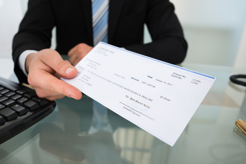Midsection of businessman giving cheque at desk in office